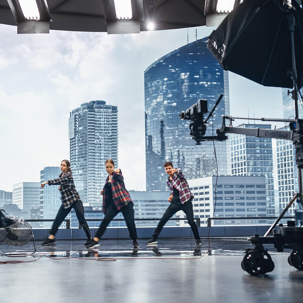 A state-of-the-art virtual production studio featuring LED wall technology that displays a realistic cityscape backdrop. Performers move across the stage while professional cameras capture the action, seamlessly blending live action with digital environments to create cinematic content.